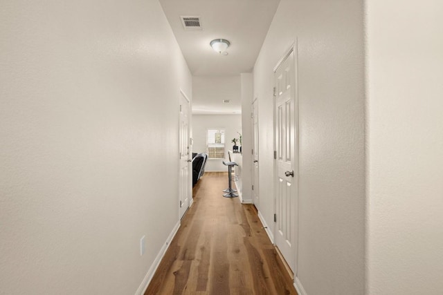 corridor featuring wood finished floors, visible vents, and baseboards