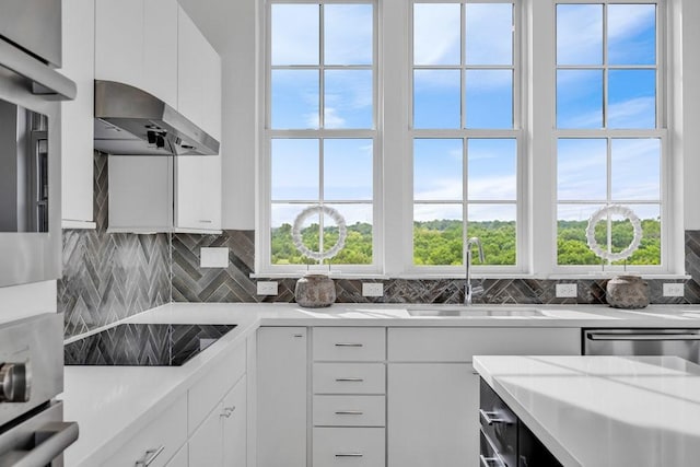 kitchen featuring a sink, decorative backsplash, light countertops, appliances with stainless steel finishes, and wall chimney exhaust hood