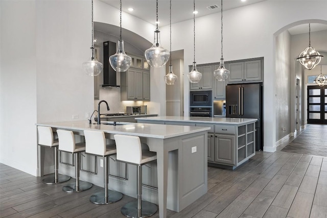 kitchen featuring stainless steel microwave, black oven, wood tiled floor, gray cabinets, and arched walkways