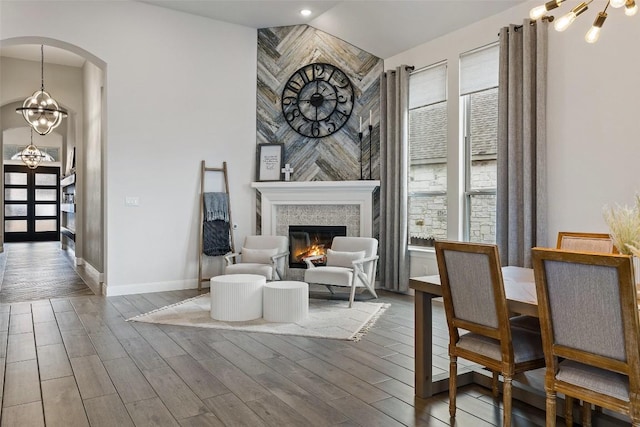 dining room with baseboards, a notable chandelier, wood finished floors, arched walkways, and a glass covered fireplace