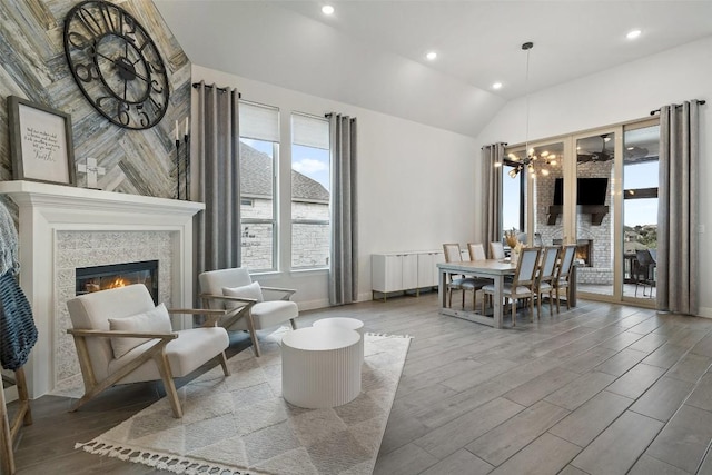 dining space with wood finished floors, an inviting chandelier, recessed lighting, a tile fireplace, and vaulted ceiling