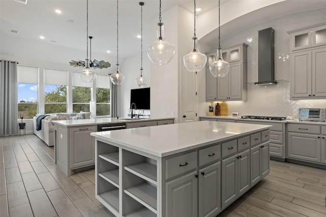 kitchen with gray cabinets, a sink, wall chimney range hood, backsplash, and a center island