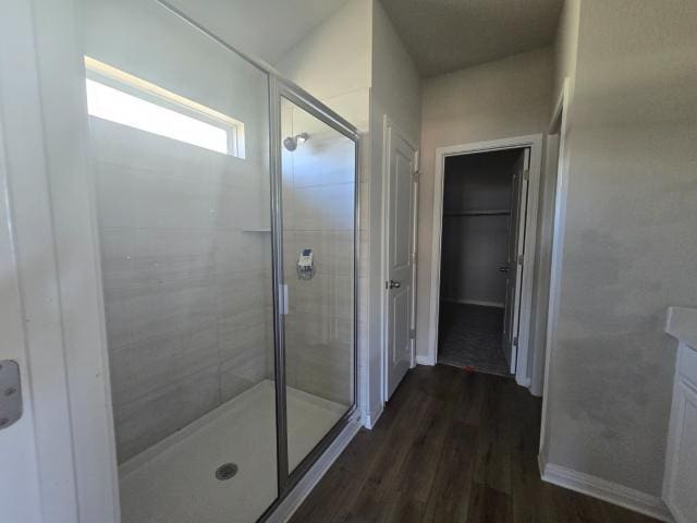 bathroom with a walk in closet, wood finished floors, and a shower stall