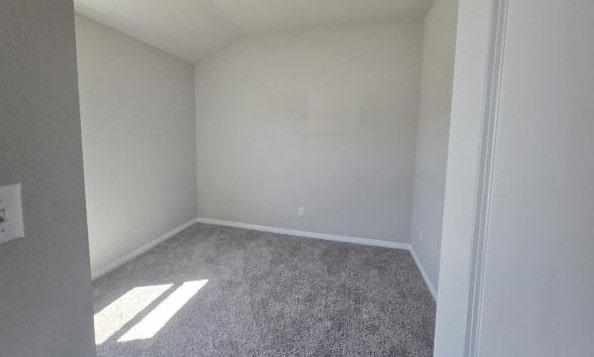 carpeted empty room featuring baseboards and lofted ceiling