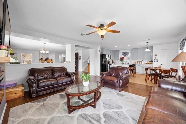 living area with visible vents, light wood-style flooring, and ceiling fan with notable chandelier