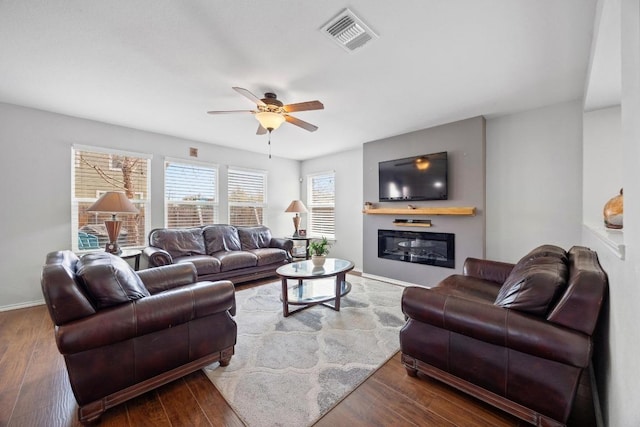 living area featuring visible vents, ceiling fan, baseboards, wood finished floors, and a glass covered fireplace