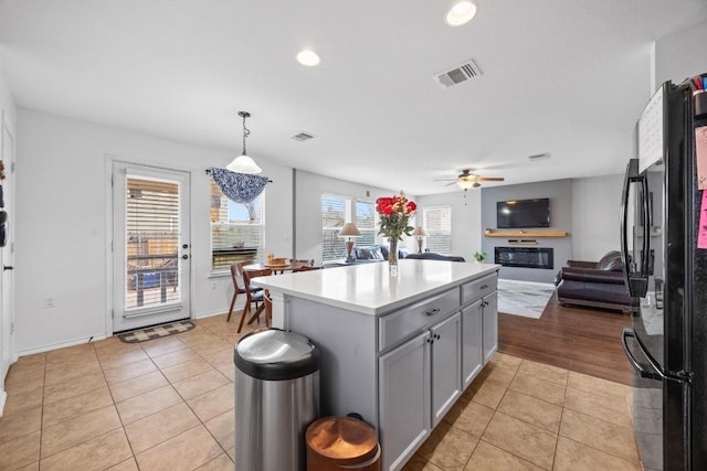 kitchen with open floor plan, light countertops, light tile patterned floors, freestanding refrigerator, and a glass covered fireplace