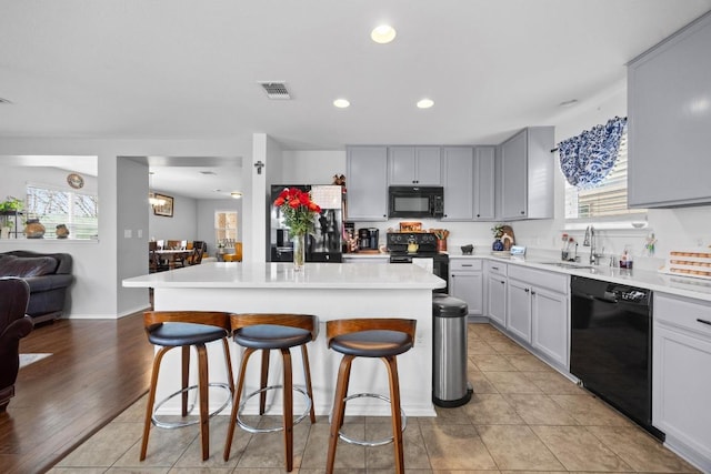 kitchen featuring visible vents, black appliances, a sink, a center island, and a breakfast bar area