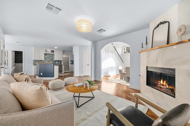 living area featuring arched walkways, visible vents, a tiled fireplace, and light wood-style floors