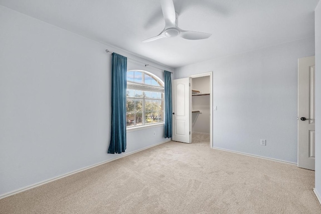 unfurnished bedroom featuring a walk in closet, light carpet, a closet, baseboards, and ceiling fan