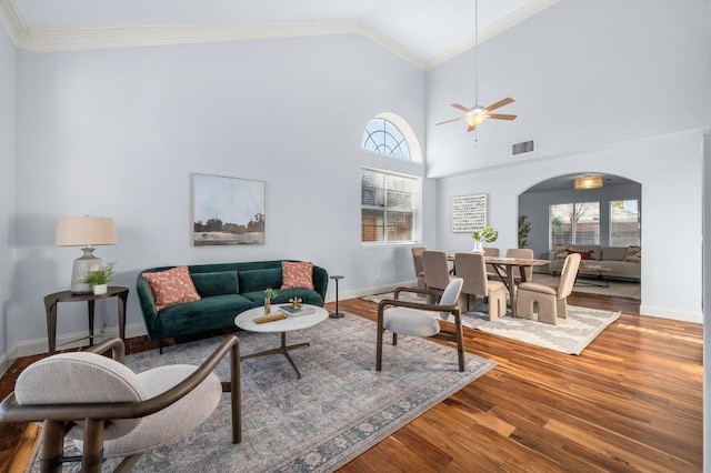 living area with crown molding, plenty of natural light, wood finished floors, and arched walkways