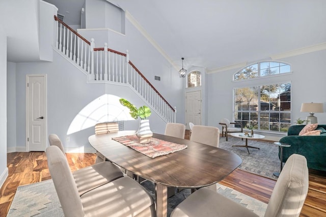 dining space with stairway, wood finished floors, a high ceiling, and ornamental molding