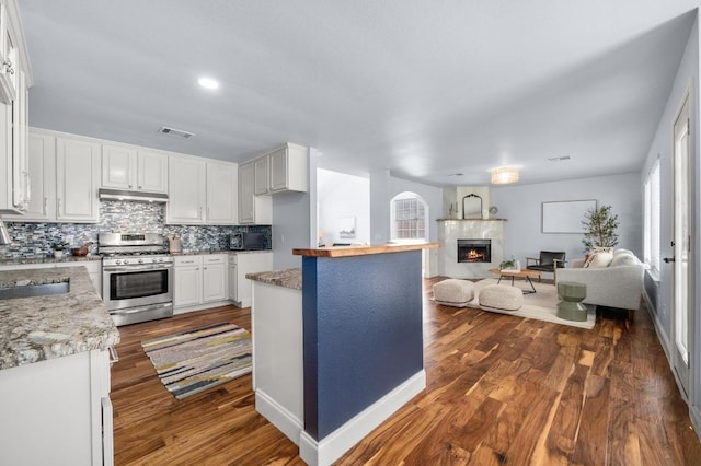 kitchen with stainless steel gas range oven, visible vents, open floor plan, a lit fireplace, and white cabinets