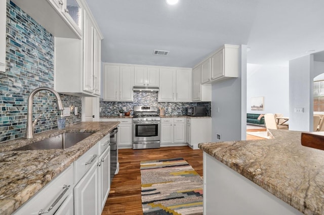 kitchen featuring visible vents, dark wood-type flooring, under cabinet range hood, gas range, and a sink