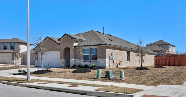 view of front of property featuring brick siding, fence, a garage, stone siding, and driveway