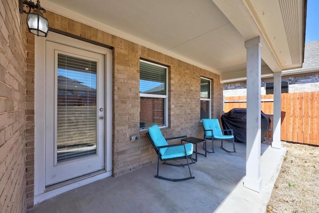 view of patio with a porch, fence, and a grill