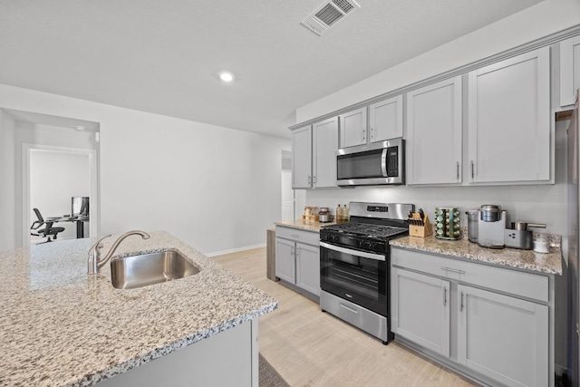 kitchen with visible vents, gray cabinets, light wood-style flooring, stainless steel appliances, and a sink