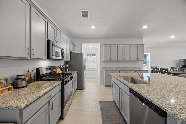 kitchen with visible vents, gray cabinets, a sink, light stone counters, and appliances with stainless steel finishes