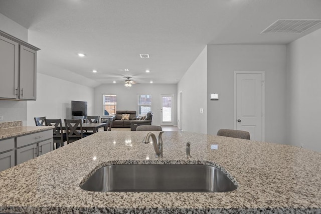 kitchen featuring light stone countertops, visible vents, gray cabinets, a sink, and open floor plan