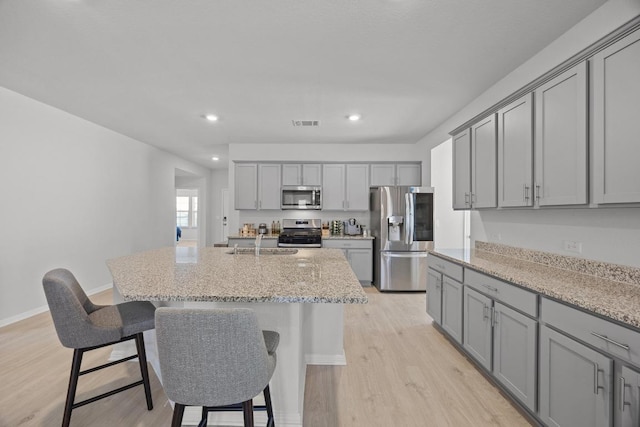 kitchen with a sink, gray cabinetry, light wood-style floors, appliances with stainless steel finishes, and a kitchen breakfast bar