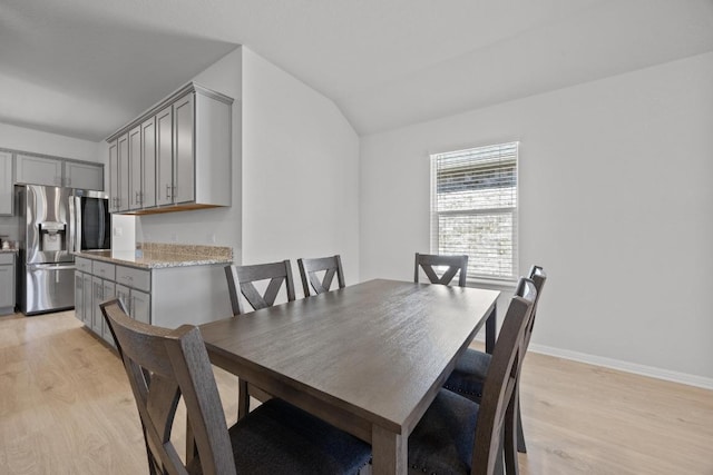 dining area featuring light wood finished floors, lofted ceiling, and baseboards