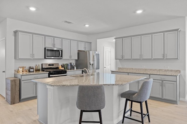 kitchen with gray cabinets, a sink, stainless steel appliances, a kitchen bar, and light wood-type flooring