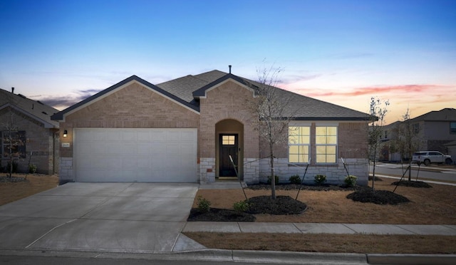 view of front of house featuring stone siding, roof with shingles, concrete driveway, an attached garage, and brick siding