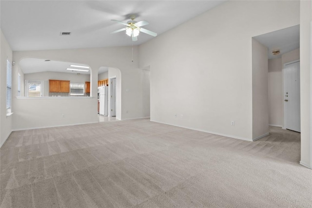 unfurnished living room with baseboards, arched walkways, ceiling fan, vaulted ceiling, and light colored carpet