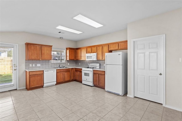 kitchen with a sink, white appliances, tasteful backsplash, and light countertops