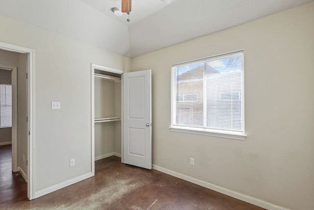 unfurnished bedroom with a closet, baseboards, lofted ceiling, and concrete floors