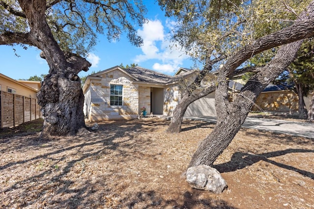 ranch-style home featuring concrete driveway, an attached garage, fence, and stone siding