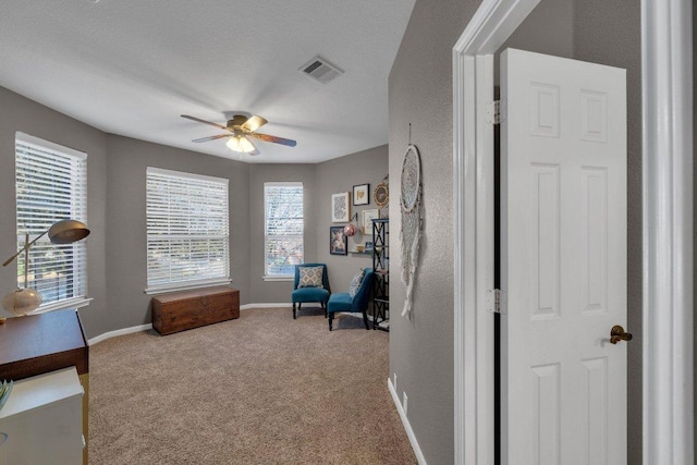 living area with visible vents, baseboards, carpet floors, a textured ceiling, and a ceiling fan