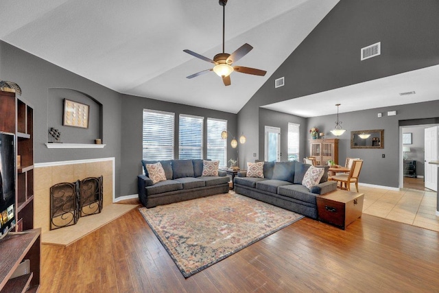 living room with visible vents, a tile fireplace, high vaulted ceiling, and wood-type flooring