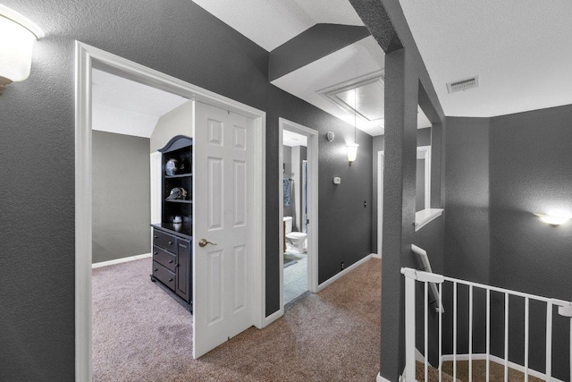 hallway featuring visible vents, baseboards, attic access, and carpet flooring