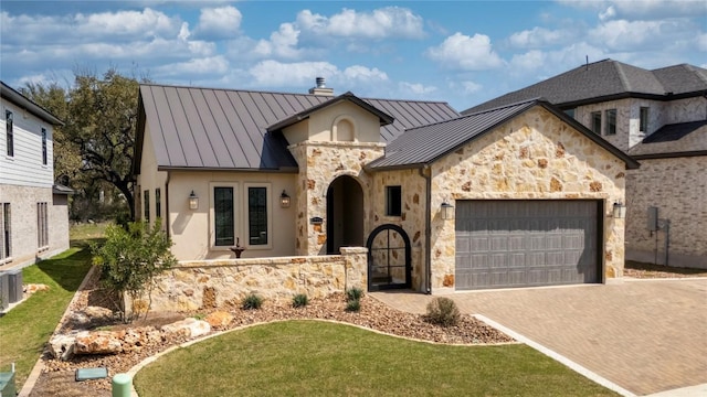 view of front facade with a chimney, metal roof, a garage, decorative driveway, and a standing seam roof