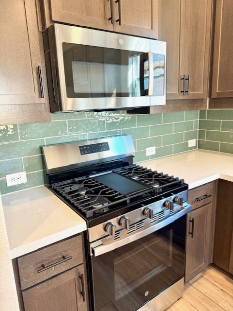 kitchen featuring light countertops, light wood finished floors, backsplash, and stainless steel appliances