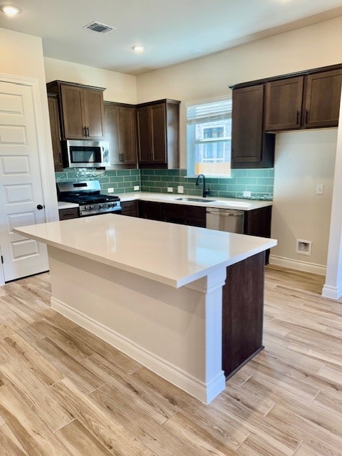 kitchen with a sink, a center island, stainless steel appliances, light wood finished floors, and dark brown cabinets