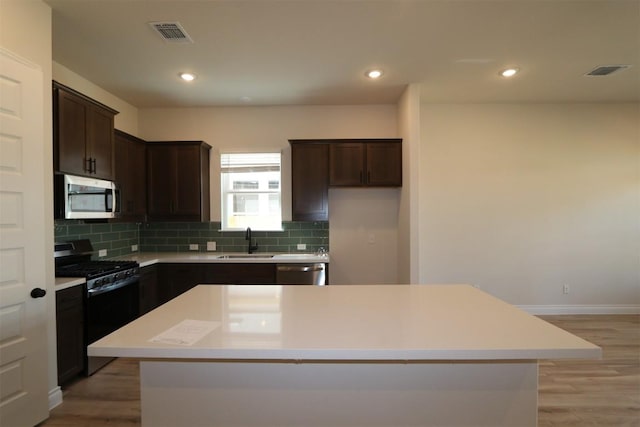 kitchen featuring visible vents, a sink, a center island, dark brown cabinetry, and appliances with stainless steel finishes