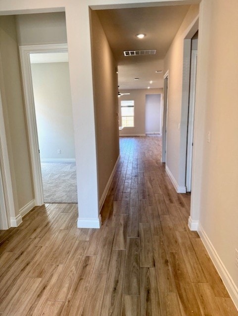 hallway featuring visible vents, baseboards, and wood finished floors