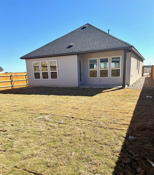 rear view of property featuring a lawn, roof with shingles, and fence