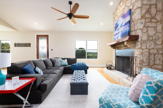 living room featuring lofted ceiling, a stone fireplace, recessed lighting, wood finished floors, and a ceiling fan