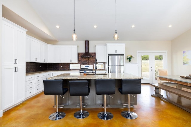 kitchen featuring finished concrete flooring, stainless steel appliances, decorative backsplash, french doors, and wall chimney range hood