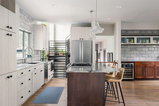 kitchen with a kitchen island, wine cooler, decorative backsplash, appliances with stainless steel finishes, and a sink