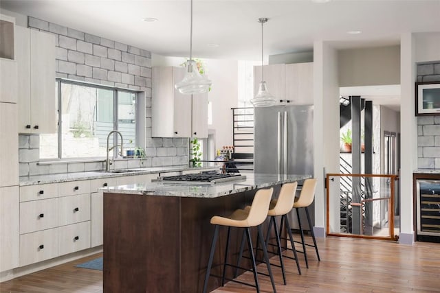 kitchen featuring tasteful backsplash, a center island, beverage cooler, wood finished floors, and a sink