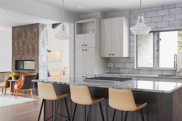 kitchen featuring tasteful backsplash, a kitchen bar, wood finished floors, gas cooktop, and a sink