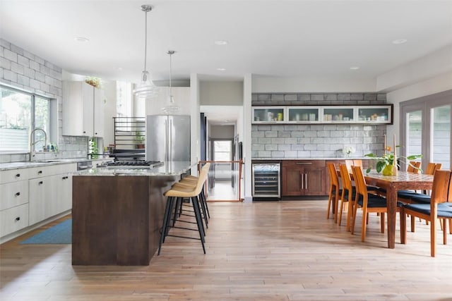 kitchen featuring beverage cooler, a sink, light wood-style floors, appliances with stainless steel finishes, and backsplash