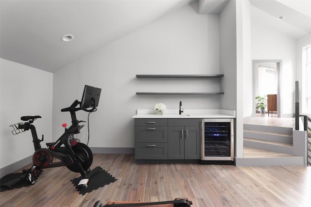 workout room with baseboards, wine cooler, light wood-style flooring, wet bar, and a sink