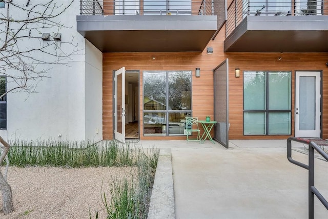 entrance to property featuring a patio, a balcony, and stucco siding