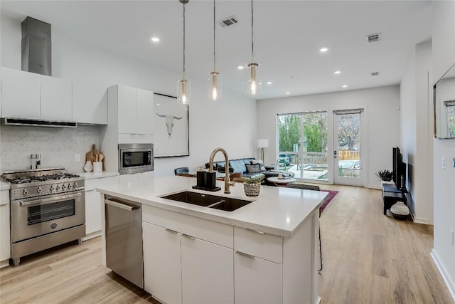 kitchen featuring visible vents, a sink, open floor plan, appliances with stainless steel finishes, and wall chimney exhaust hood