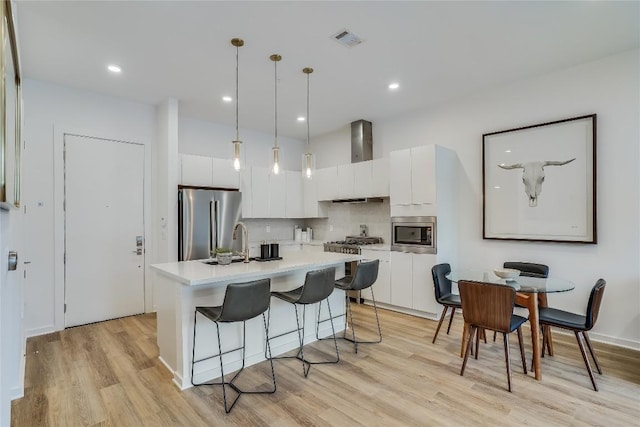 kitchen with visible vents, light countertops, appliances with stainless steel finishes, white cabinets, and wall chimney exhaust hood